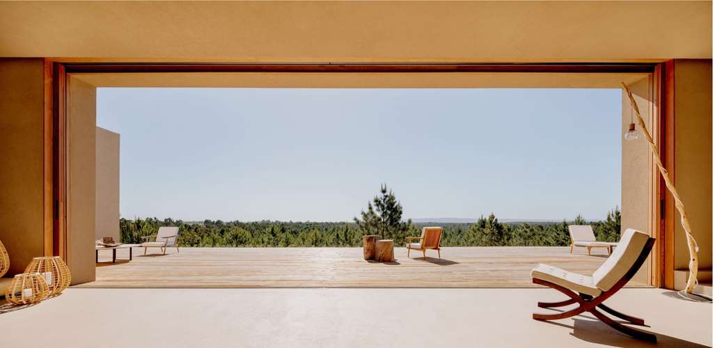 Open living area framing a pine forest view, with lounge chairs on the floor