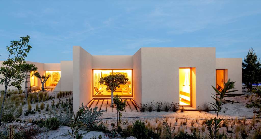 Cream house with glowing windows and a desert garden at blue hour