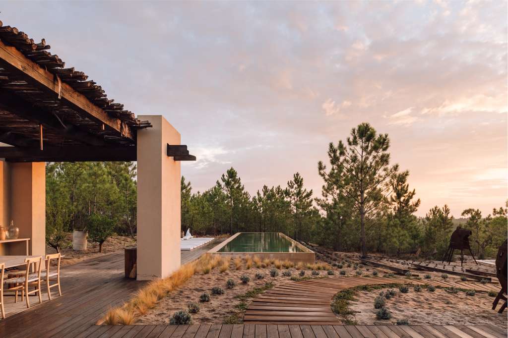 Terrace with a timber pergola overlooking pine trees and a pool at sunset