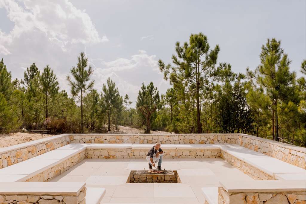 Person crouching in a sunken stone seating circle among pine trees