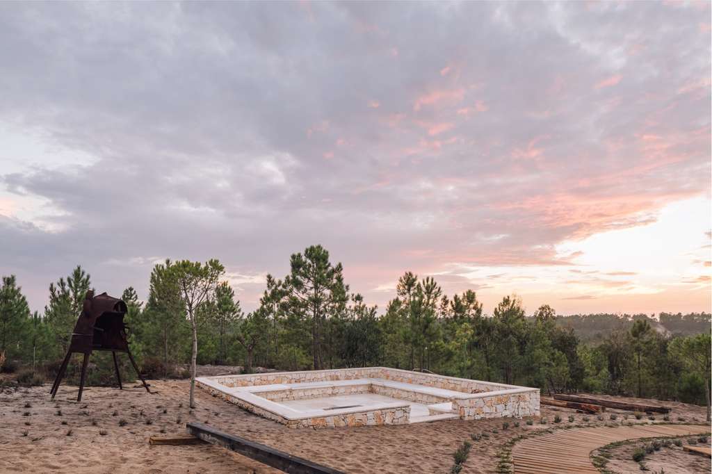 Sunken stone amphitheatre and rusted sculpture in dunes at dusk