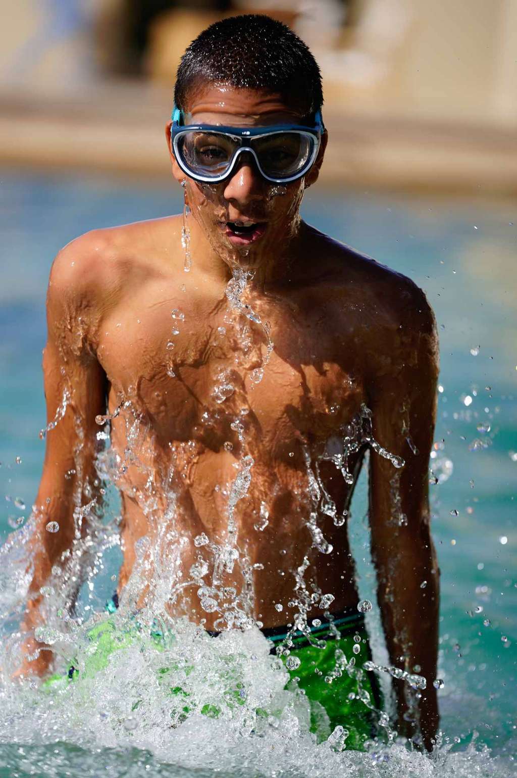 Boy in swimming goggles rising from splashing pool water