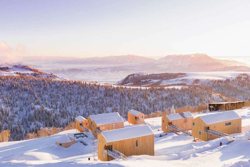 Bloomberg article photo of snow-covered wooden cabins in mountains at sunset