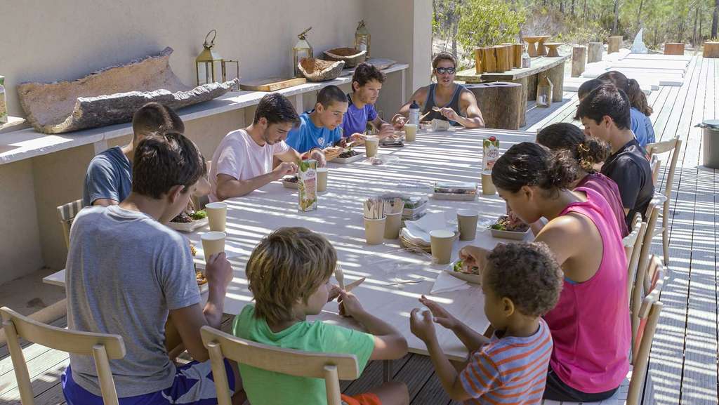 Children seated at a long table on a wooden terrace