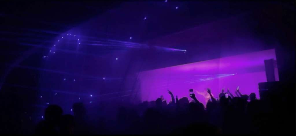 Concert crowd with raised hands under purple stage lights
