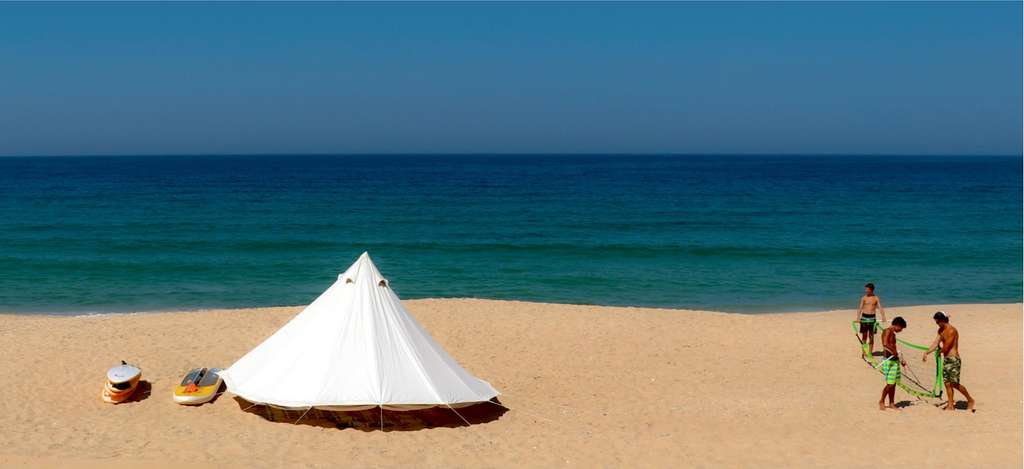 White tent on a beach with people carrying a board near the sea