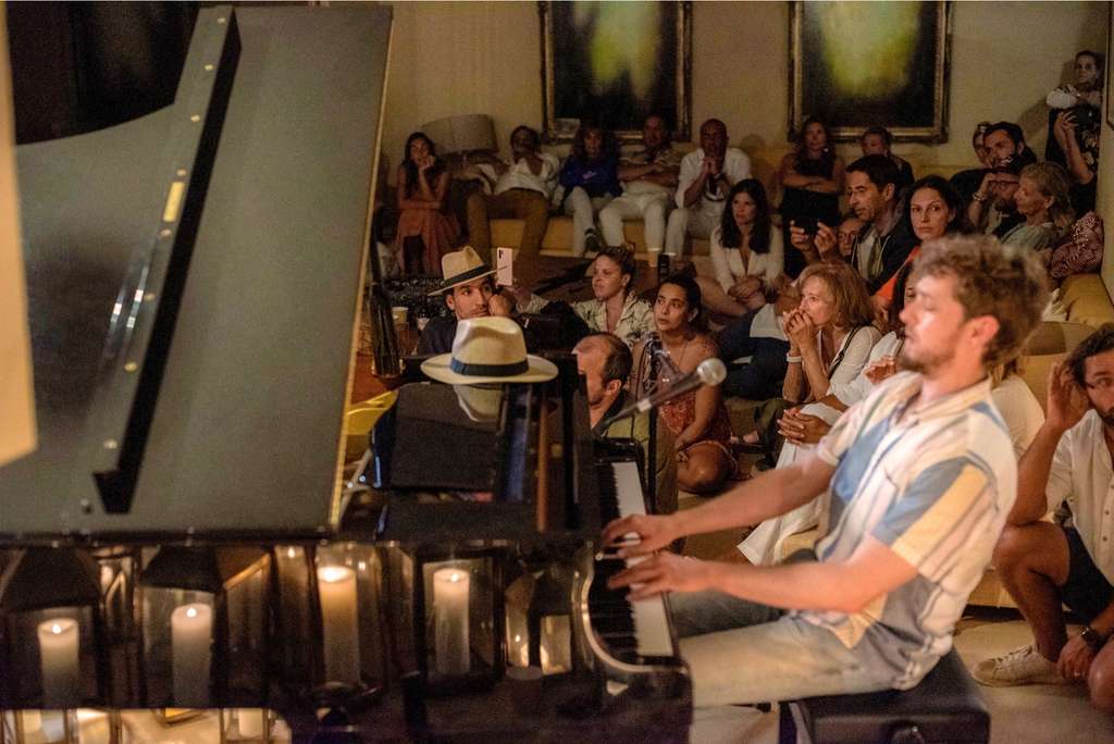 Man playing a grand piano in front of a seated audience by candlelight