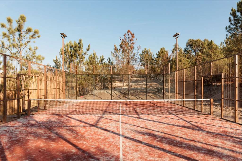 Padel court with red clay surface surrounded by pine trees