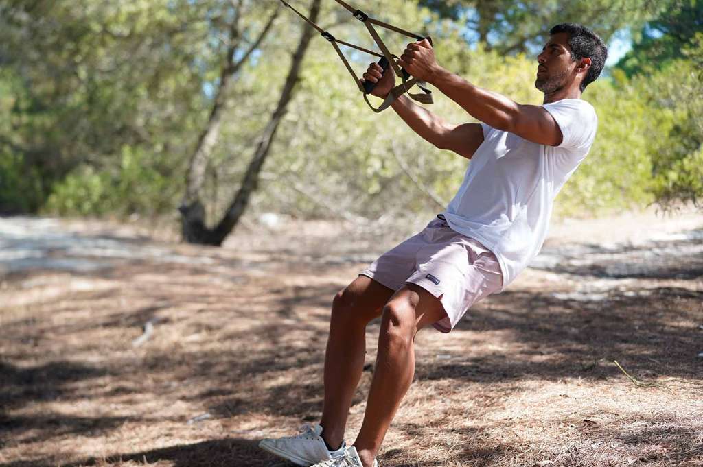 Man leaning back on suspension straps hung from a pine tree
