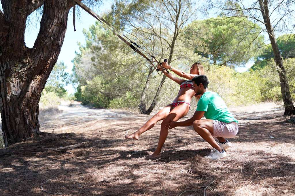 Woman and man doing a suspension training exercise under pine trees