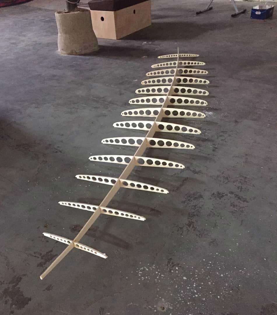 Wooden surfboard frame with oval cutouts on a workshop floor