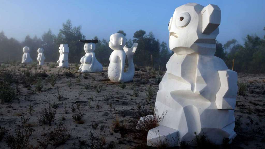 White monkey-like sculptures standing in misty dunes