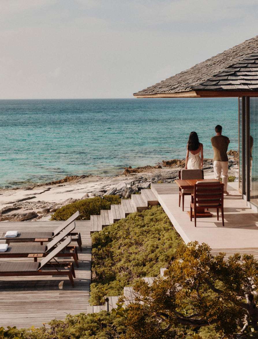 Two people on a seaside villa terrace overlooking turquoise water
