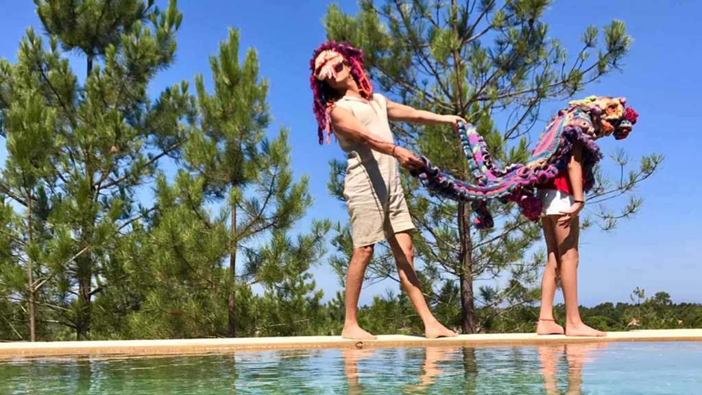 Two people in crocheted costumes stretching a long cloth beside a pool
