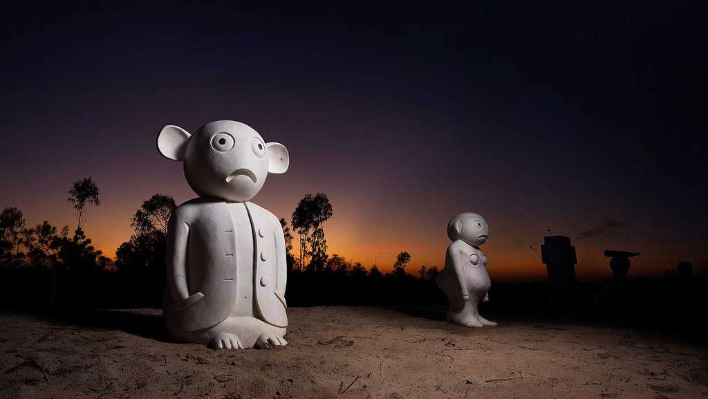 Two white stone cartoon-like figures in dunes at dusk