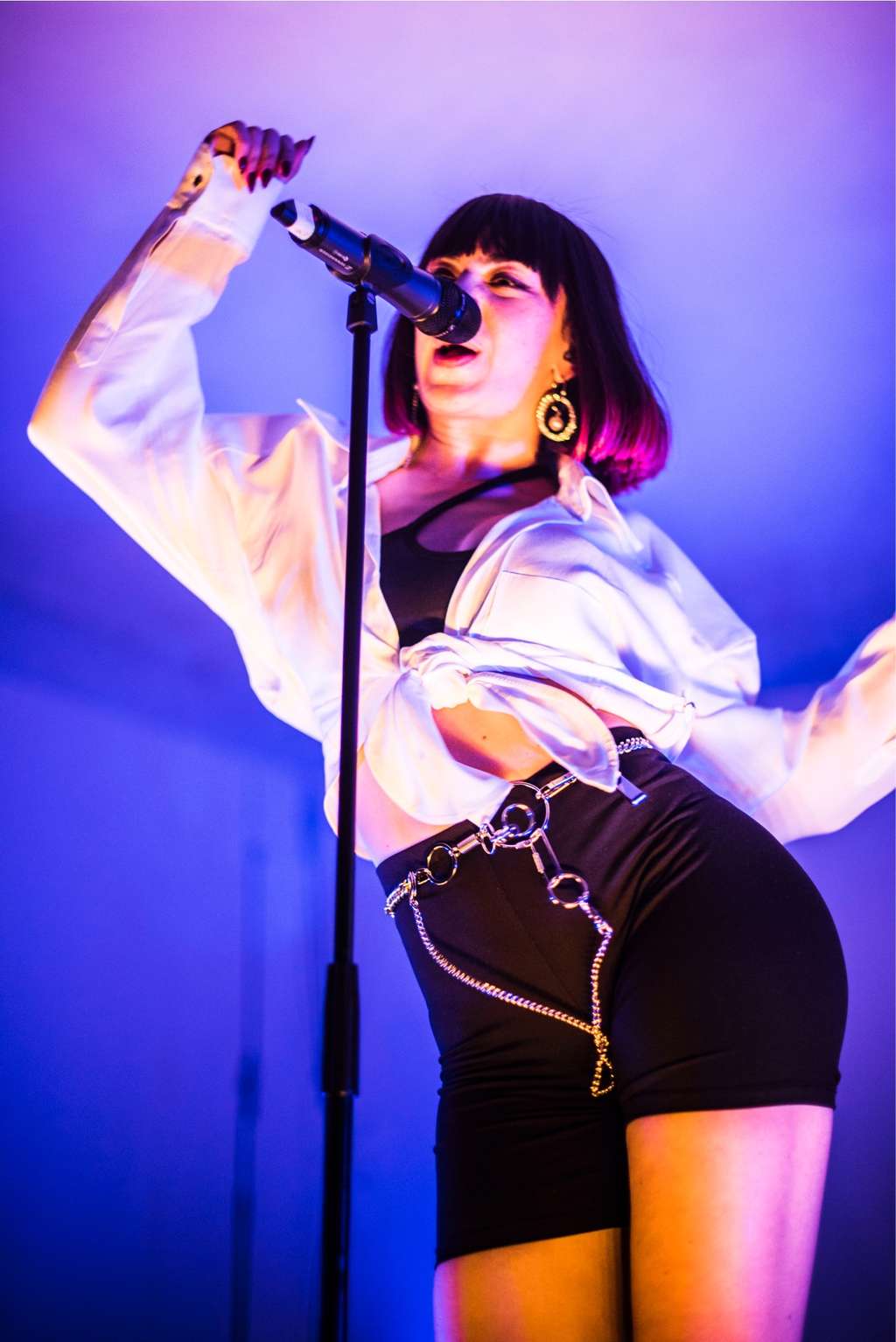 Singer in a white jacket and shorts performing under blue and purple light