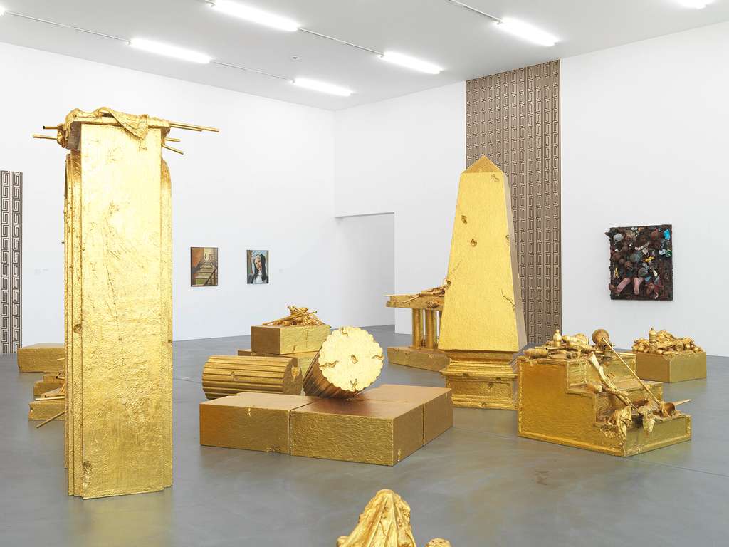 Gallery with golden sculptures and obelisks and small paintings on the walls