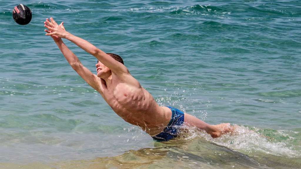 Boy diving for a ball over shallow sea water
