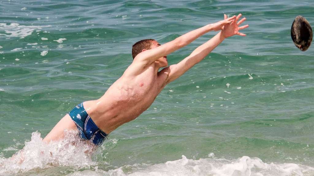 Boy stretching to reach a ball as he splashes into the sea