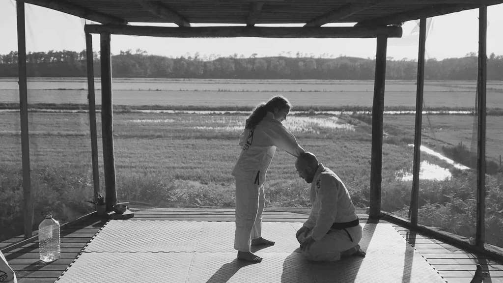 Black and white photo of two people bowing on a mat by a rice field