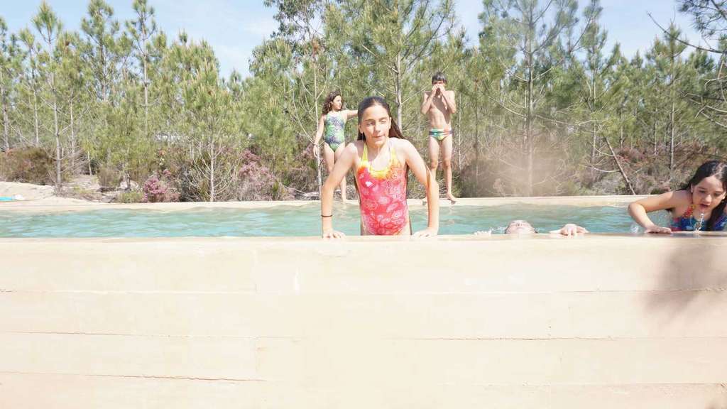 Girl in a pink swimsuit at the edge of a pool among pines