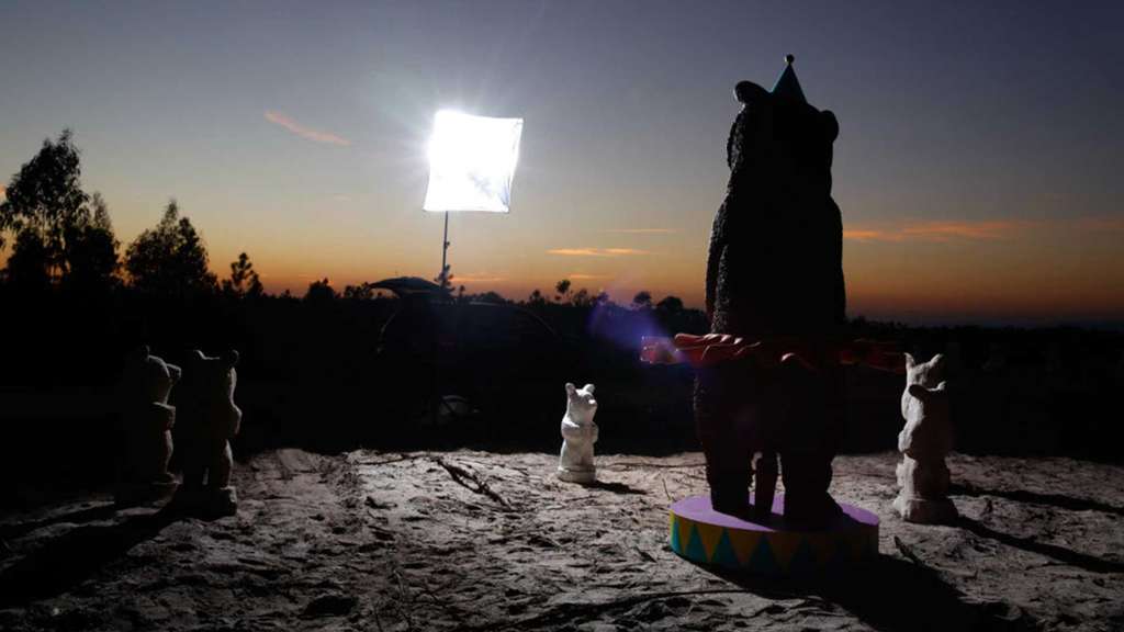 Bear sculpture in a party hat silhouetted at dusk beside a studio light