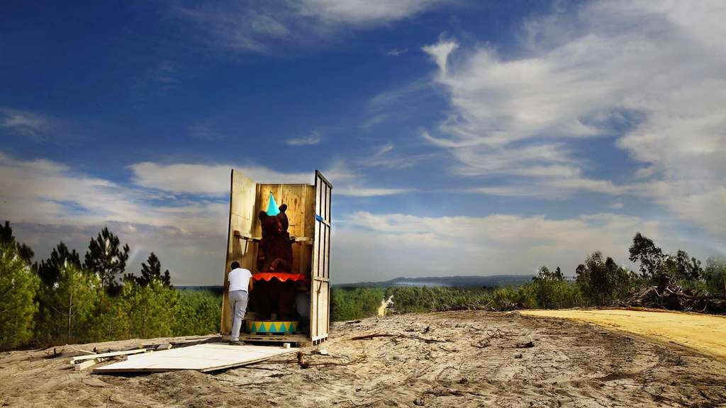 Person opening a wooden booth on a hilltop under a blue sky