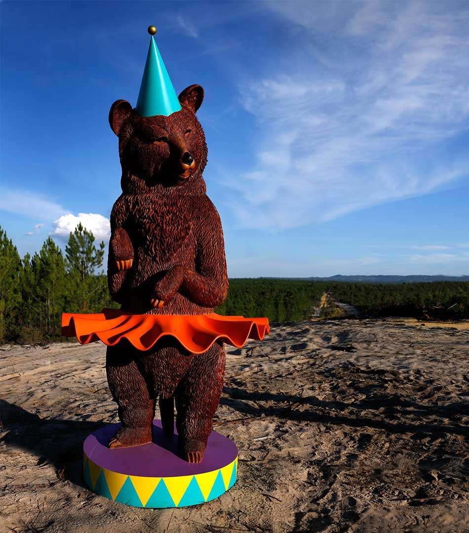 Brown bear sculpture in an orange skirt and party hat on a podium
