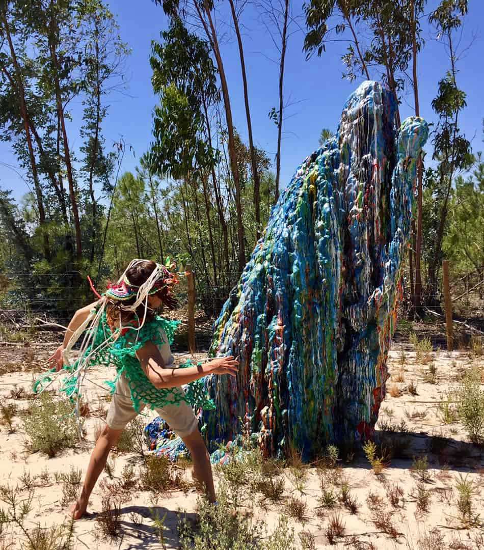 Person in a crocheted costume dancing beside a large blue woven sculpture